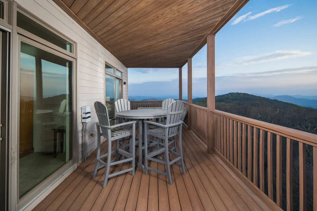 An inviting wooden deck equipped with an outdoor dining set, framed by majestic mountains and open sky. The setup suggests sociable evenings or peaceful moments spent watching the sunset or stargazing from the comfort of the deck.