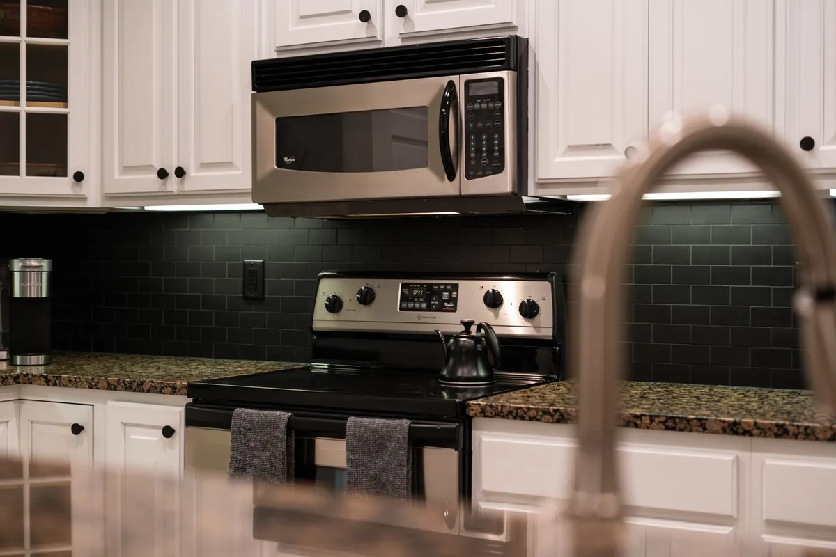 This image offers a close-up perspective of the kitchen, featuring a sleek black stove, stainless steel microwave, granite countertop, and colorful kitchen towels. The warm lighting and layout reinforce the kitchen’s functionality and cozy feel for home-cooked meals.