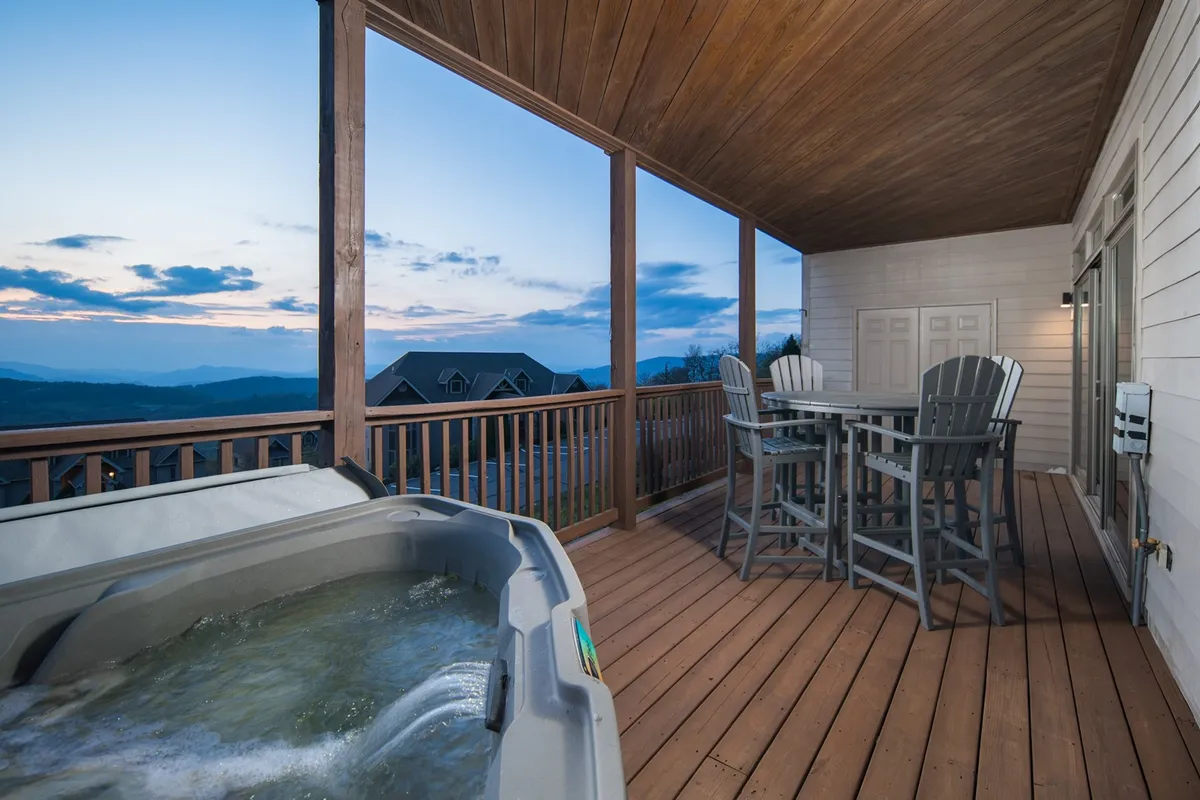 A tranquil outdoor scene featuring the hot tub and an outdoor dining set on the deck, both overlooking the expansive mountain landscape. The image exudes a peaceful ambiance, perfect for relaxing soaks or al fresco dining with unmatched views.