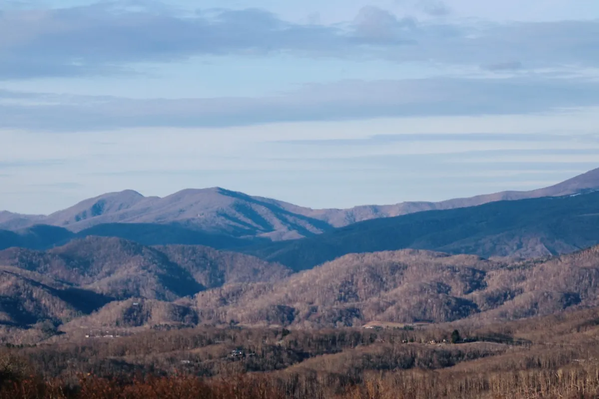 A sweeping view of Sugar Mountain's scenic mountain ranges and valleys under a vast sky, capturing the region's natural beauty and seasonal changes. The landscape evokes feelings of adventure, tranquility, and connection with nature—ideal for showcasing outdoor exploration, foliage tours, and year-round festivities.