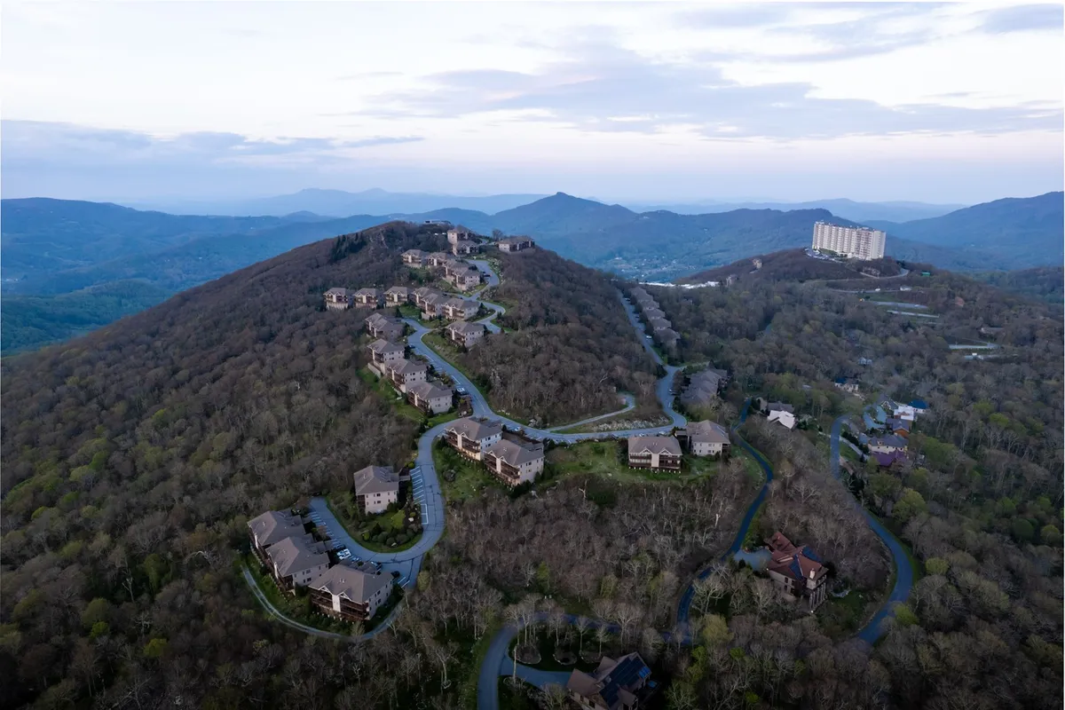 A tranquil exterior scene featuring a picturesque mountainous landscape, residential structures nestled among the hills, and winding roads inviting exploration. The setting basks in soft natural light, hinting at both summer and winter possibilities for outdoor fun.