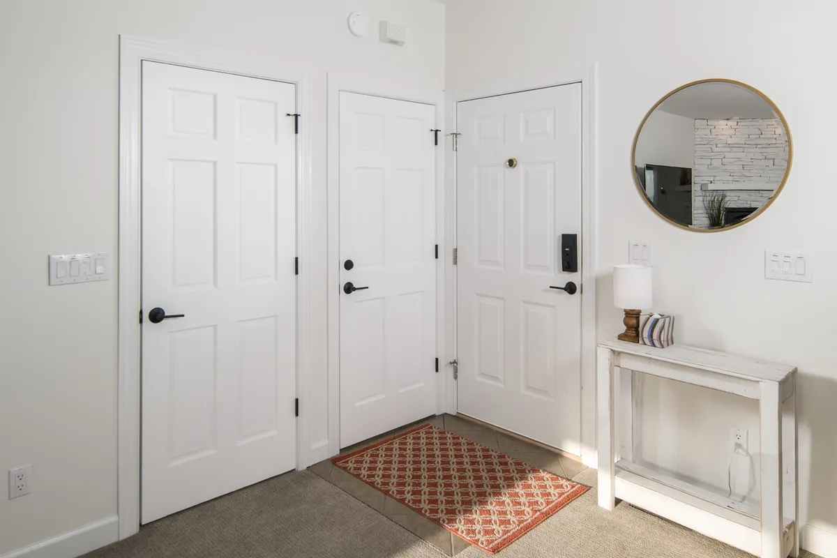An inviting entryway with three white doors, a round mirror, and a small console table. The scene suggests a welcoming return to the condo after a festive day out, with space for guests to hang coats and drop off items, creating a sense of comfort and arrival.