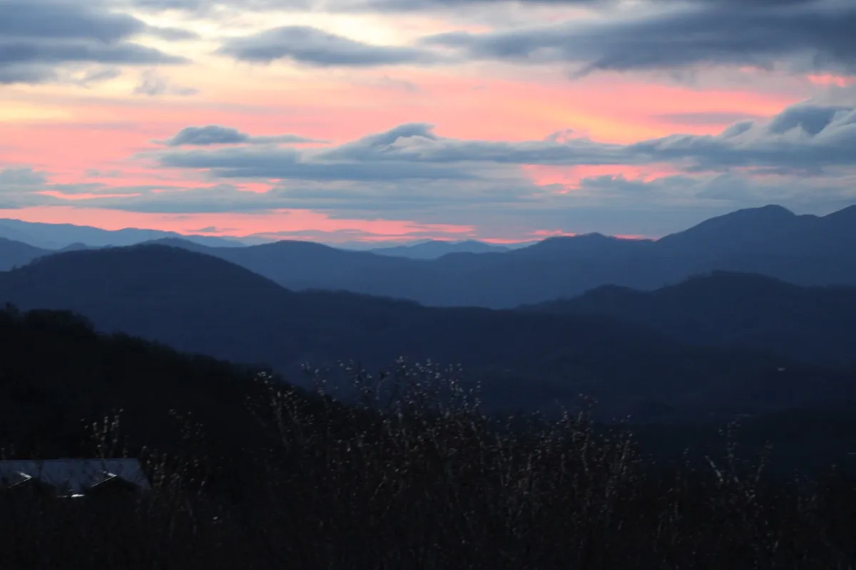 This view image captures the silhouettes of distant mountains under a colorful, expansive sky, with hints of clouds catching the evening light. The scene evokes a sense of vastness and tranquility, inviting viewers to imagine the outdoor adventures that await just beyond the property.